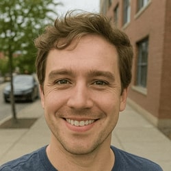 Man smiling outdoors with a building and car in the background