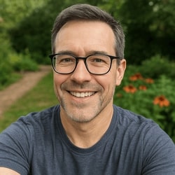 Man wearing glasses and a blue shirt with a blurred natural background